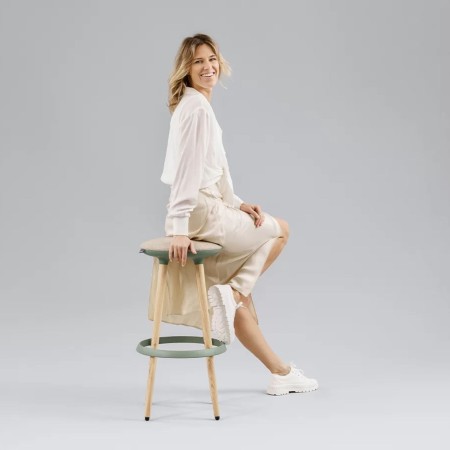 Femme assise sur un tabouret Cannie en pose dynamique sur fond gris – Cannie