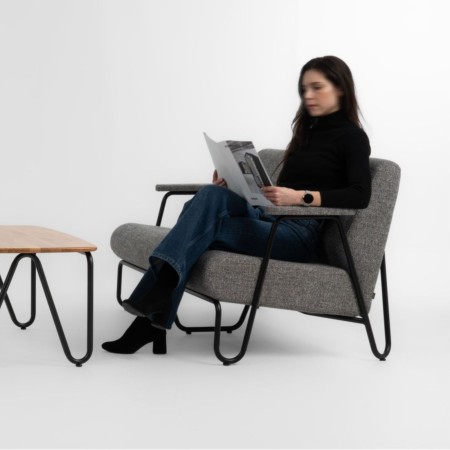 Fauteuil Clip en tissu gris avec accoudoirs bois, occupé par une personne lisant – Clip