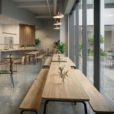 Aménagement de cafétéria d’entreprise moderne avec tables et bancs industriels en bois et acier à Neuchâtel.