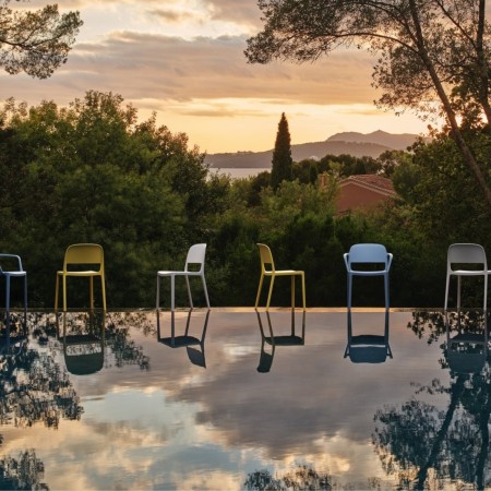 Chaises Blendy avec et sans accoudoirs en plusieurs coloris installées au bord d’une piscine extérieure.